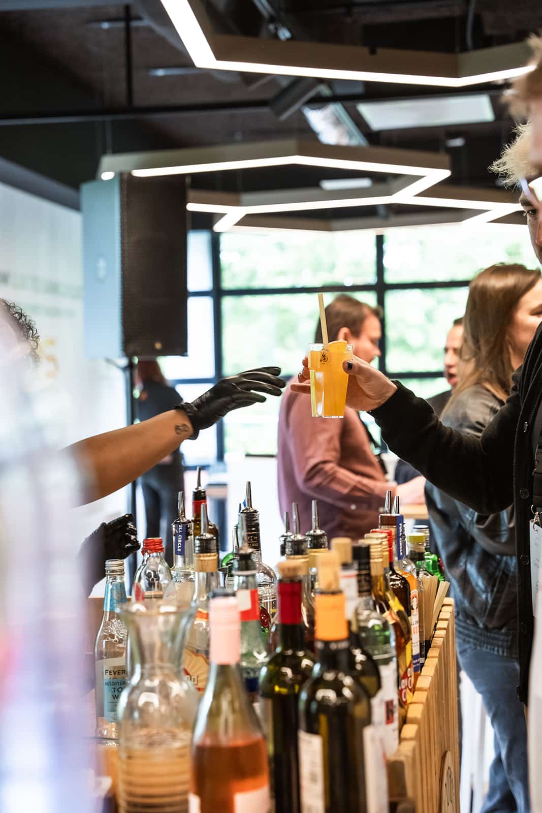 Bartender vult oranje spritz in wijnglas met ijs op de houten bar van De Cocktailfiets in een lichte kas