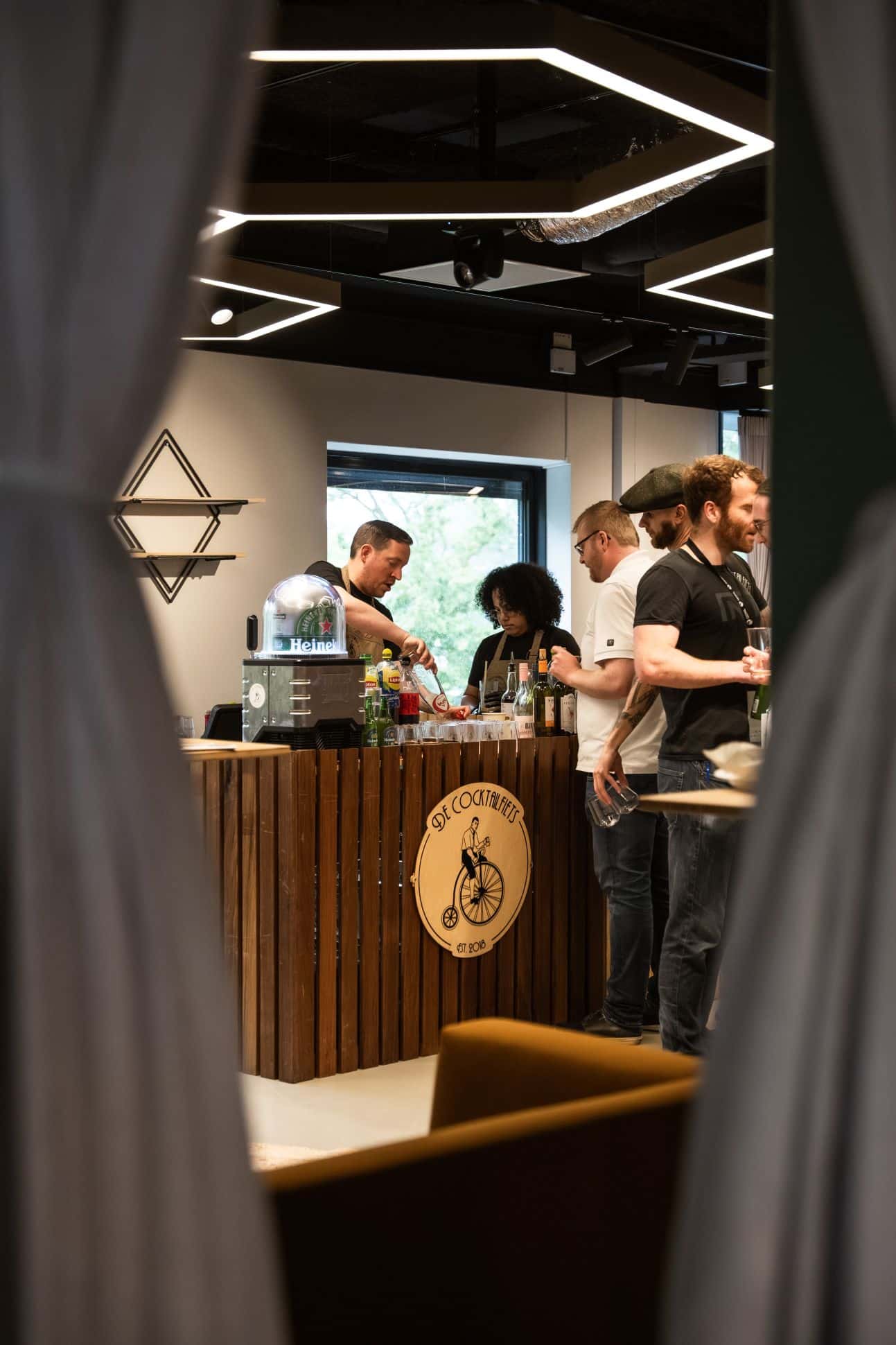 Persoon draagt donkerkleurige De Cocktailfiets-sweater met geborduurd borstlogo, gefotografeerd bij de bar